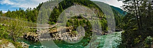 Panoramic view of a river in Montana wilderness with a cable bridge over water