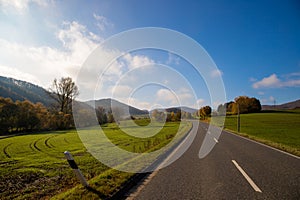 Panoramic view on a road with green meadows blue sky, in autumn with forest