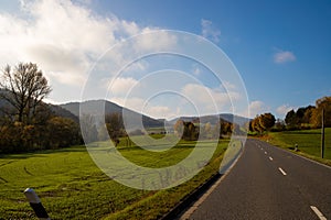 Panoramic view on a road with green meadows blue sky, in autumn with forest