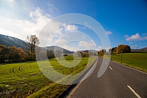 Panoramic view on a road with green meadows blue sky, in autumn with forest