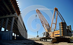 A panoramic view of a road overpass under construction and a yellow crawler crane in the morning sun