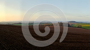 Panoramic view of rolling english countryside with blue sky and green fields and brown muddy ploughed fields