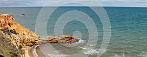 view of a sandstone cliff face with a stone wave breaker poking out into the bay around Melbourne, Victoria, Australia