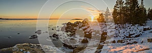 Panoramic view of Scenic Winter Sunset over sea, big stones at coastline and forest of peninsula Kont, Umea, Sweden. Winter