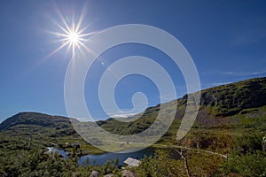 Panoramic view of a small town in mountains with lake, blue sky, bright sun and no cloud