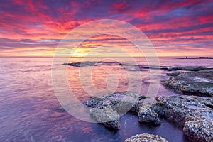 Panoramic view of a smooth sea and a rocky shore during a beautiful sunset