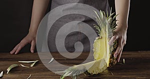 Panoramic view to falling quarter of fresh ripe pineapple on a wooden table. Girl`s hands hold natural exotic fruit.