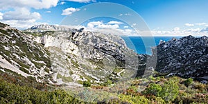 A panoramic view to a rocks and a road leading through a valley to a turquoise sea