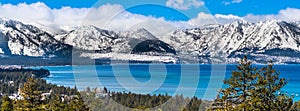 Panoramic view towards Lake Tahoe on a sunny clear day; the snow covered Sierra mountains in the background; evergreen forests in
