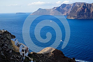 Panoramic view of vast blue Aegean seascape and caldera background with sailing ship and building along island foreground from Oia