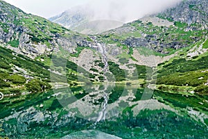 Panoramatický výhled na vodopád a jezero s průhlednou čistou vodou poblíž Sliezského domu. Odraz krajiny v