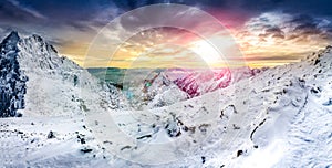 Panoramatický výhled na bílé zimní hory při barevném západu slunce
