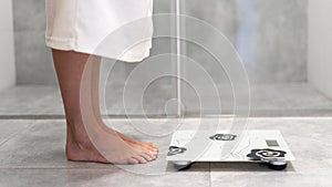 Woman in white bathrobe standing on weigher