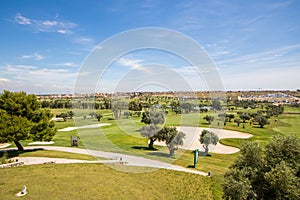 Panoramic views of golf course with sandpit, lake, trees and buggies