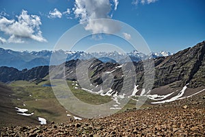 Panoramic vista from a mountain summit showcasing a range of snow-dusted peaks, a clear blue sky overhead, and a serene alpine