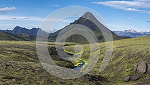 Panoramic volcanic landscape of green Storasula mountain with lush moss and blue creek water between Emstrur and