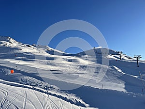panoramic winter landscape with clear blue sky, empty freshly groomed ski slopes and a chair lift