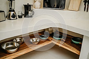 Pans and stainless stell bowls on wooden shelf. Bright white modern design of luxury kitchen