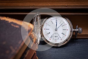 Panta rhei concept: antique pocket watch and pile of vintage hard cover books on natural stone