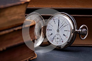 Panta rhei concept: antique pocket watch and pile of vintage hard cover books on natural stone