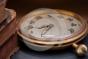 Panta rhei concept: antique pocket watch and pile of vintage hard cover books on natural stone