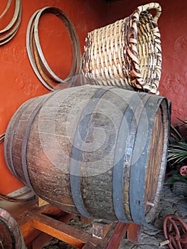 Pantry with old wine barrel and wicker basket to collect grapes.Wicker basket with handles on a wine barrel on red background.