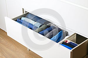 Pants folded according to the method of Marie Kondo. Vertical storage of clothes in a chest of drawers. Storage organization.
