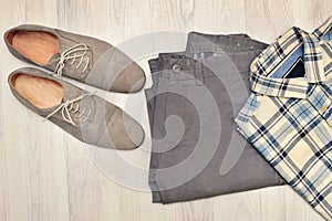 Pants, plaid shirt and gray suede shoes. Overhead view of men`s casual outfits on white wooden background.