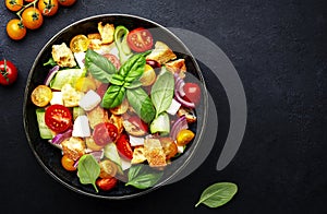 Panzanella salad with stale bread, colorful tomatoes, mozzarella cheese, onion, olive oil, salt and green basil, black table