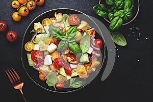 Panzanella salad with stale bread, colorful tomatoes, mozzarella cheese, onion, olive oil, salt and green basil, black table