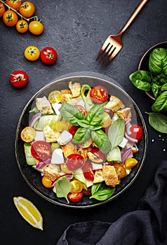 Panzanella salad with stale bread, colorful tomatoes, mozzarella cheese, onion, olive oil, salt and green basil, black table