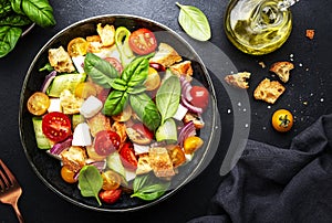 Panzanella salad with stale ciabatta bread, colorful tomatoes, soft cheese, red onion, olive oil, sea salt and green basil, black