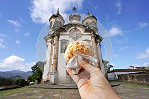Pao de queijo (Brazilian cheese bun) with the church of St. Francis of Assisi in Ouro Preto, Minas Gerais, Brazil