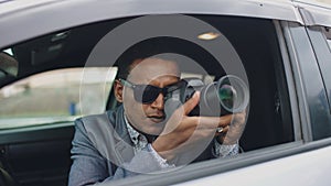 Paparazzi man sitting inside car and photographing with dslr camera