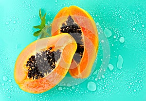 Papaya fruit on blue background with water drops, fresh exotic fruits border design. Halves of fresh organic Papaya