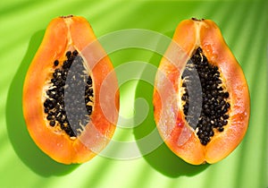 Papaya fruit on tropical green background with shadows of palm tree. Halved fresh organic Papayas