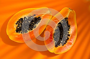 Papaya fruit on tropical orange background with shadows of palm tree. Halved fresh organic Papayas