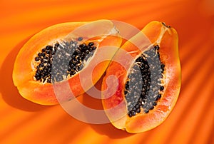 Papaya fruit on tropical orange background with shadows of palm tree. Halved fresh organic Papayas