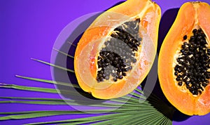 Papaya fruit on tropical violet background with palm tree leaf. Halved fresh organic Papayas