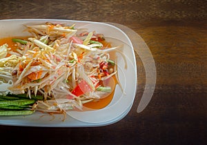 Papaya salad cooked with cowpea, peanut, carrot, lemon, chilis and sugar on white plate food long beans Wood Table Texture.