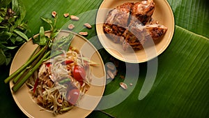 Papaya salad Somtum serving with Thai style grilled chicken on banana leaves background