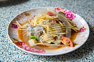 Papaya salad, which put Pickled Fish and long beans. Papaya salad in white dish on wooden background.