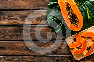 Papaya slices on dark wooden background top view copy space