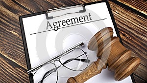 Paper with AGREEMENT with gavel  pen and glasses on the wooden background