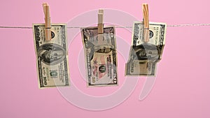 Paper american dollars hang on a clothesline, attached with a wooden clothespin. Pink background, money laundering concept