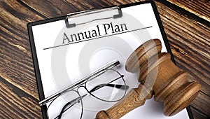 Paper with ANNUAL PLAN with gavel, pen and glasses on wooden background