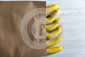 Paper bag of bananas on white wooden background.