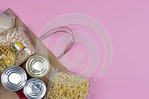 Paper bag with a crisis food supply for the period of quarantine isolation on a pink background with a copy of space, pasta, oatme