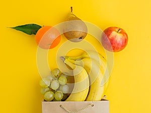 Paper bag of different health food on yellow background. Top view. Flat lay. A brown paper shopping bag with fruits