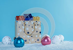 A paper bag filled with gifts stands in the snow. Christmas decorations.